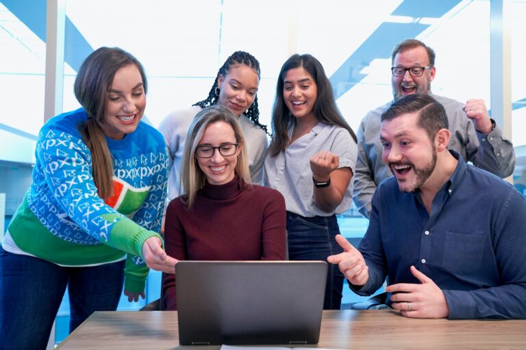 men and women sitting and standing while staring at laptop