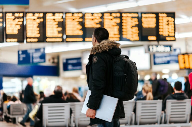 man standing inside airport looking at LED flight schedule bulletin board